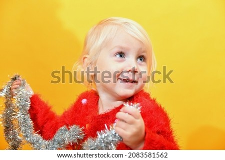 A little girl in a red sweater decorates the tree with festive toys and glittering tinsel.