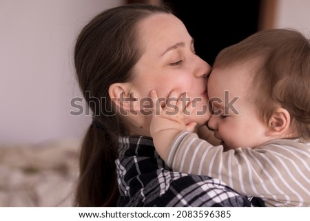 Portrait Adorable Face Of Little Cheerful Happy Toddler baby girl child With Charming Smile Look At Mom Strong Cuddles Loving Mommy Together. Mother Hugs play love care kiss smiling daughter at home