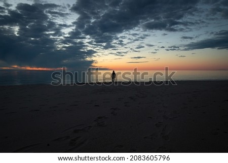 A man walks silhouetted on the beach of lake superior at sunset