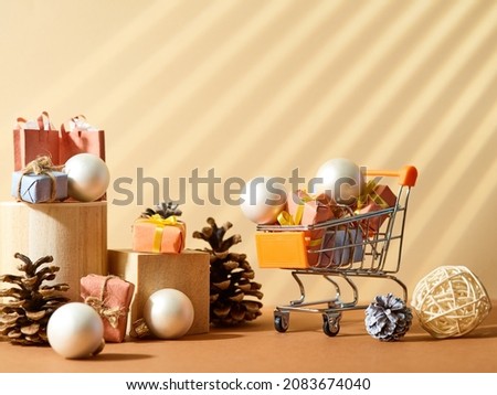 The original composition is a small souvenir shopping cart with purchases, Christmas balls, cones on a beige background. Christmas and New Year discounts, sales, online shopping.