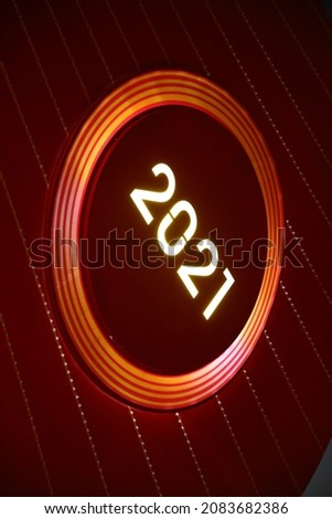 New Year neon sign on dark red background.   2021 glowing text in Christmas ball electric led lamp  with light sparkles.