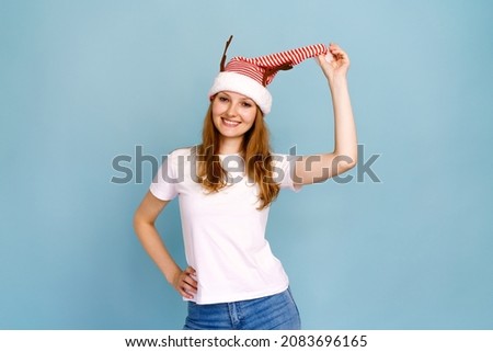Portrait of an excited smiling caucasian girl dressed as christmas deer and white t-shirt, smiling cheerfully and posing, on a blue background. Cheerful young woman christmas and new year concept
