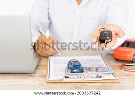 Close-up shot of hand of agent handing car keys to the customer after signing a car rental and purchase contract form