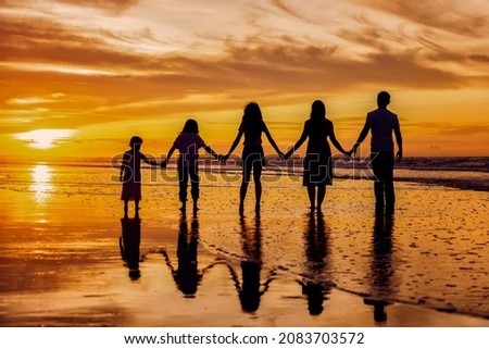 Silhouettes of big happy family holding the arms each other's on beach during golden sunset