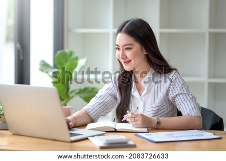 Pretty young Asian businesswoman working on laptop and taking notes In office.	