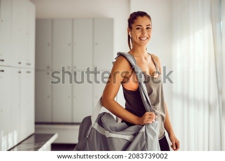 Young female athlete with sports bag standing in dressing room in a gym and looking at camera. Copy space. Royalty-Free Stock Photo #2083739002