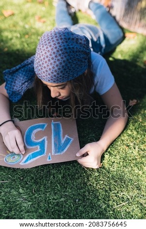 Teenage girl activist painting a protest sign in the garden on a spring day. Drawing an appeal to prevent the Earth's temperature from rising by 1.5 degrees Celsius.