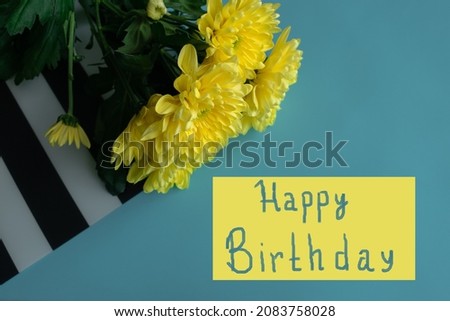 A bouquet of yellow chrysanthemums on a blue background on a striped napkin. In the yellow field it says Happy Birthday. Bright image of flowers. A greeting card.