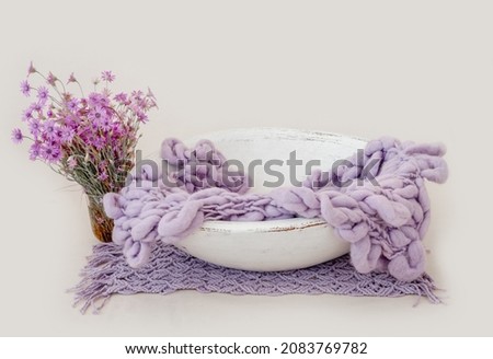 Wooden basin decor for newborn studio photoshoot filled with knitted blanket closeup. Infant baby photo furniture and flower bouquet