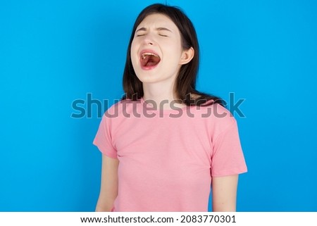 Caucasian woman wearing pink T-shirt over blue background angry and mad screaming frustrated and furious, shouting with anger. Rage and aggressive concept.