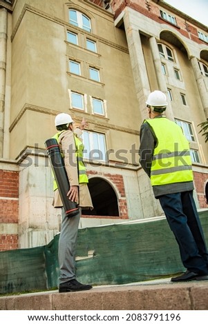 Two senior construction workers are standing and looking at the building