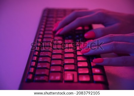 Unrecognizable woman with vivid orange manicure working on wireless keyboard in neon light, view of hands.
