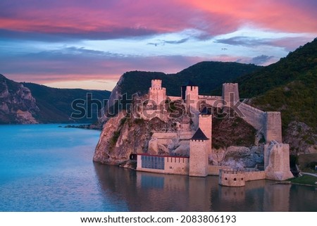 Aerial, iew of the medieval fortress Golubac over  Danube river. Fortress towers illuminated by pink light. Sunset, pink and red clouds sky. Outdoor and traveling castle theme. Serbia. Royalty-Free Stock Photo #2083806193