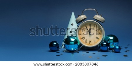 Alarm clock with party hat and Christmas balls on blue background with space for text