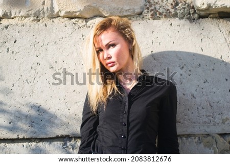 Attractive young woman dressed in a gray blank shirt posing against the background of a concrete wall in the rays of the setting sun 