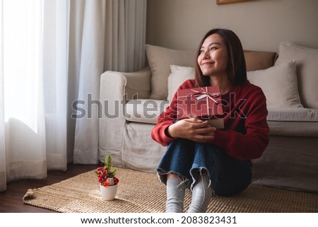 Portrait image of a young woman holding and receiving a red present box at home