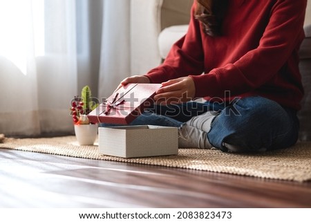 Closeup image of a young woman opening a gift box at home