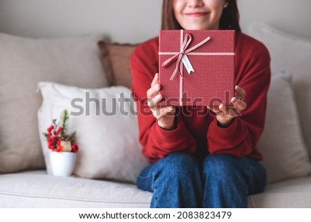 Closeup image of a young woman holding and showing a red present box 
