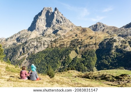 Family day at the mountains in  french Pyrenees. Father, mother and baby sitting on a meadow while enjoy views of Pic du Midi d'Ossau. Mountain travel vacation.