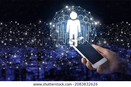 Human search.Leader and CEO. Hand hold white smartphone with digital hologram Human, Leader sign on city dark blurred background. Human resources and team management concept