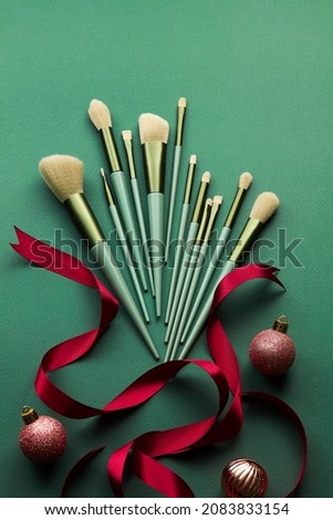 Green makeup brushes decorate with christmas ornament red ribbon in green background for advertising , top view and product holiday content