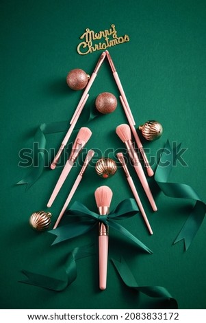 Pink makeup brushes decorate with christmas ornament green ribbon in green background for advertising , top view and product holiday content