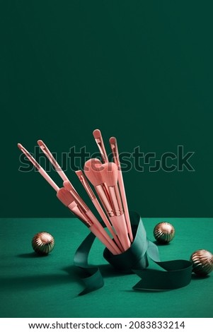 Pink makeup brushes decorate with christmas ornament green ribbon in green background for advertising , front view and product holiday content