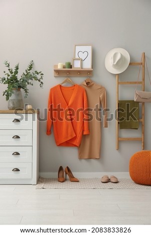 Modern room interior with stylish wooden furniture, fashionable clothes and shoes