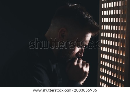Young priest in confession booth Royalty-Free Stock Photo #2083855936