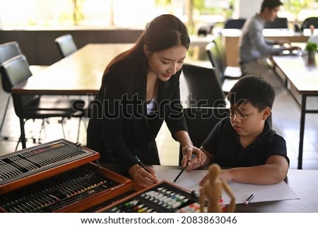 Smiling asian teacher helping children coloring picture in art class