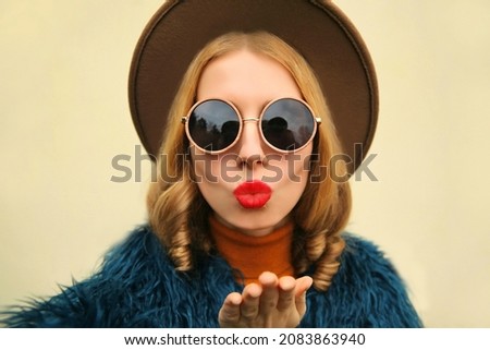 Fashionable portrait of stylish young woman stretching hand for taking selfie blowing her lips with red lipstick sending sweet air kiss