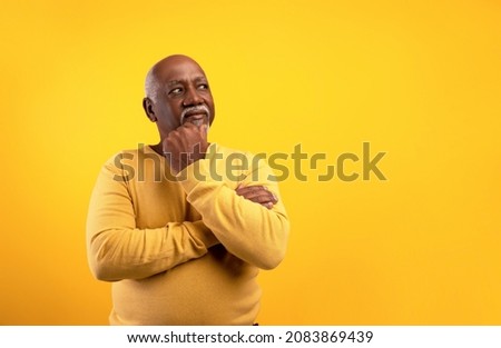 Thoughtful senior African American man looking aside at empty space, touching his chin, deep in thought on orange studio background. Dreamy elderly black male offering place for your advertisement Royalty-Free Stock Photo #2083869439