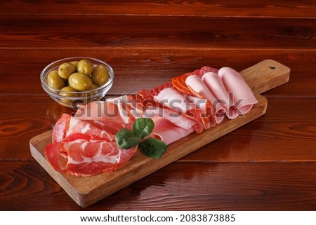 Sliced smoked meat appetizers are served on a cutting board. There are large green olives nearby.