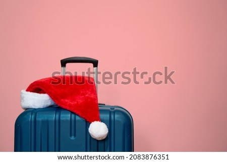 Blue plastic suitcase with Santa Claus hat over pink pastel background. Concept of travel and visit relatives on Christmas Holidays           Royalty-Free Stock Photo #2083876351