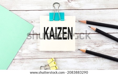Stickers with pencils and notebook with text KAIZEN on the wooden background
