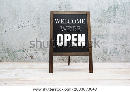 Welcome We're Open typography text on the blackboard set on wooden floor and brick background