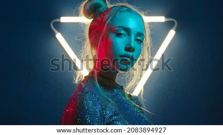 Young woman looking at the camera in the neon light of the club. Camera zoom. Portrait of a beautiful futuristic girl close-up. Lady in multicolor glow. Royalty-Free Stock Photo #2083894927