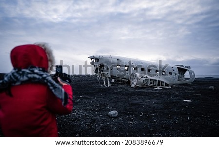 Girl taking a picture the abandoned DC-3 Airplane on Solheimasandur beach. Airplane wreckage on black sand beach. Douglas Dakota DC3, US navy, South Iceland.