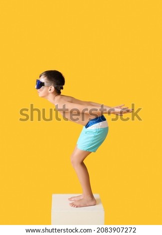 Little boy in start position on swimming block against color background