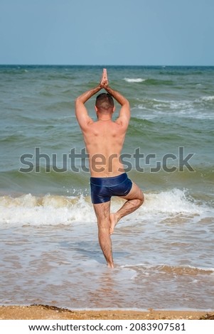 Full body shot of the man doing yoga on a beach