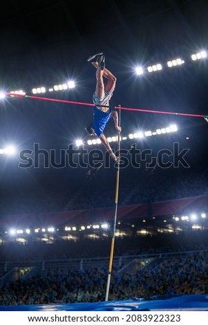 Pole Vault Jumping: Professional Male Athlete on World Championship Successfully Jumping with Pole over Bar. Shot of Competition on Big Stadium with Sports Achievement Experience Royalty-Free Stock Photo #2083922323