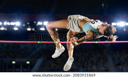 High Jump Championship: Professional Female Athlete on World Championship Successfully Jumping over Bar. Shot of Competition on Stadium with Sports Achievement Experience. Determination of Champion. Royalty-Free Stock Photo #2083931869