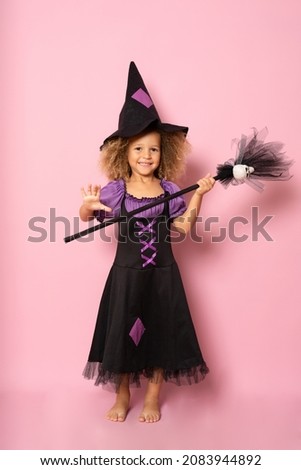 Little girl posing in a witch costume isolated over pink background.