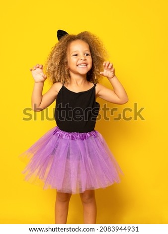 Little girl posing in a halloween costume isolated over yellow background.