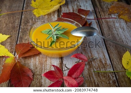 pumpkin soup in a glass bowl on a wooden table decorated with autumn colorful leaves