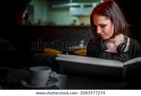 young teenager redhead girl student drawing with pencil in paper album sitting in cafe