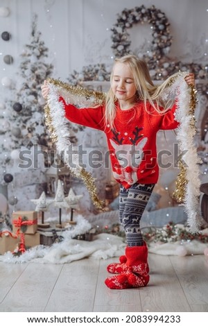 Little girl wearing christmas clothes, spinning in the living room near the fireplace and the Christmas Tree, dancing.  Child spinning around in the hall with Christmas decorations