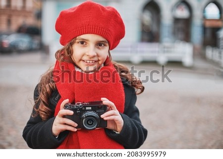 beautiful smiling girl in a red beret and scarf takes pictures on the city street. High quality photo