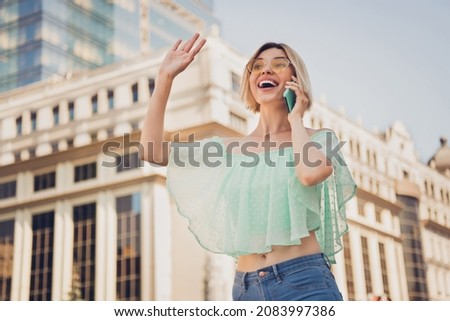 Photo of cool millennial blond lady talk telephone wave wear teal blouse spectacles outsite in city