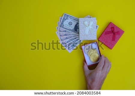 Hand holds a new year gift of money and bitcoin on a yellow background.